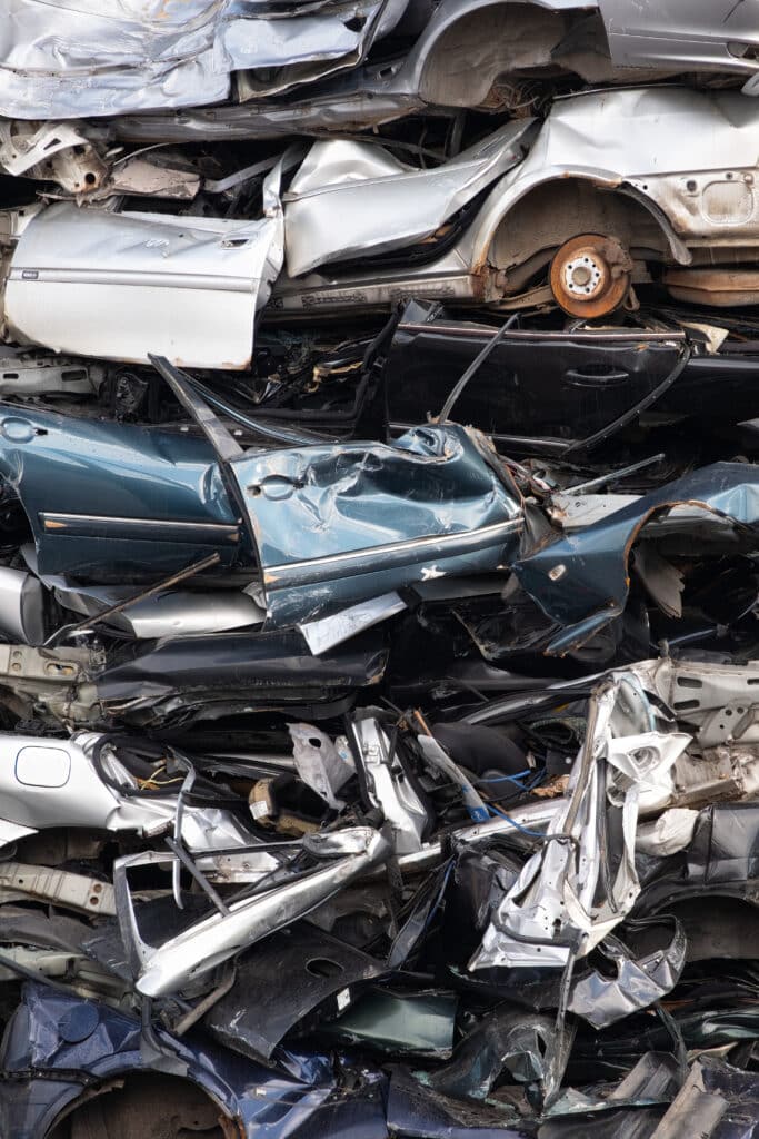 Ferraille de voitures accidentées empilées : recyclage Grosse pile verticale de carcasses de voitures accidentées et écrasées, pièces tordues métalliques argentées, bleues et noires.